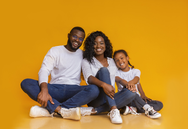 Χαμογελώντας αφρικάνικη οικογένεια κάθεται στο πάτωμα πάνω από κίτρινο φόντο στούντιο - Φωτογραφία, εικόνα