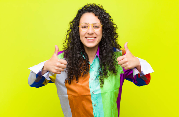 young pretty woman smiling broadly looking happy, positive, confident and successful, with both thumbs up against chroma key wall - Zdjęcie, obraz