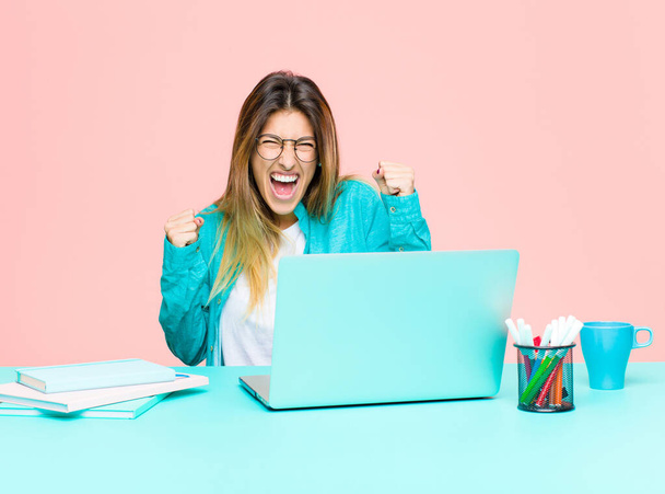 young pretty woman working with a laptop feeling happy, positive and successful, celebrating victory, achievements or good luck - 写真・画像