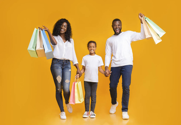 Eltern und ihre Tochter tragen Einkaufstüten und lächeln - Foto, Bild