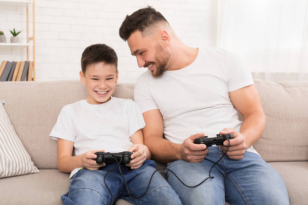 Ο μπαμπάς και ο γιος με χειριστήριο παίζουν βιντεοπαιχνίδια στο σπίτι. - Φωτογραφία, εικόνα