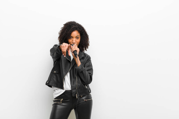 young pretty black woman with a microphone wearing a leather jacket against white wall - Фото, изображение