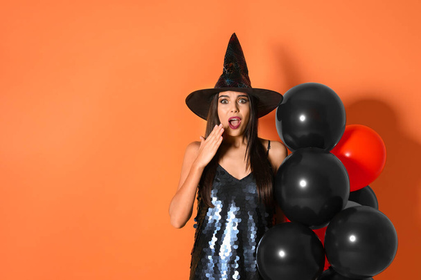 Surprised woman wearing witch costume with balloons for Halloween party on yellow background, space for text - Foto, Imagem