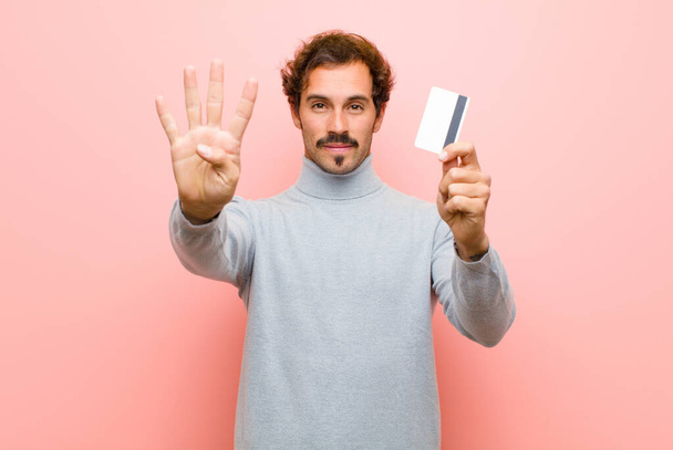 young handsome man with a credit card against pink flat wall - Фото, изображение