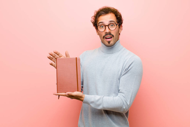 young handsome man with a note book against pink flat wall - Foto, Bild