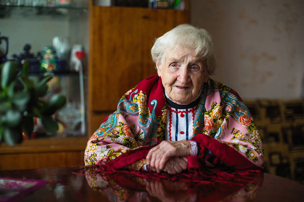 An elderly woman in bright clothes and a scarf sitting at the table. - Photo, Image