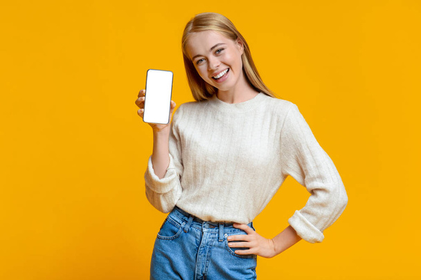 mooi tiener meisje presenteren smartphone met blanco scherm voor mockup - Foto, afbeelding