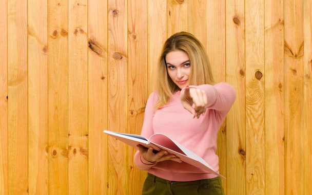 young pretty blonde woman with books against wood wall - Fotografie, Obrázek