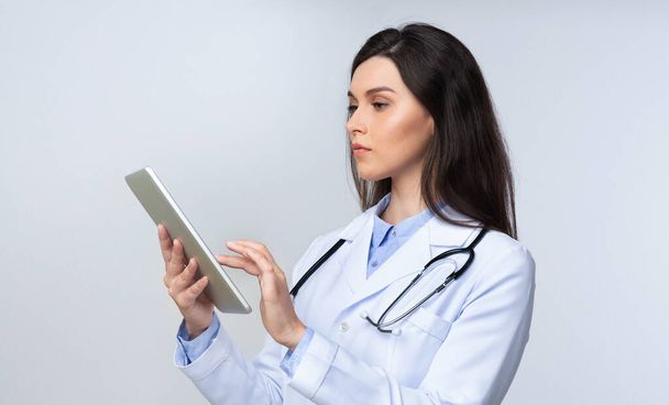 Medico donna utilizzando tablet computer in piedi su sfondo grigio
 - Foto, immagini