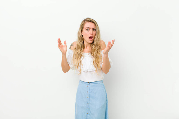 young blonde woman looking shocked and astonished, with jaw dropped in surprise when realizing something unbelievable against white wall - Photo, image