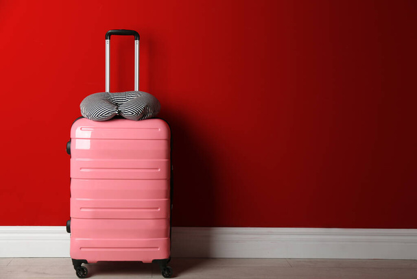 Pink suitcase and striped travel pillow near red wall, space for text - 写真・画像
