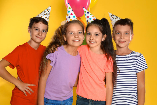 Niños felices en sombreros de fiesta sobre fondo amarillo. Celebración del cumpleaños
 - Foto, imagen
