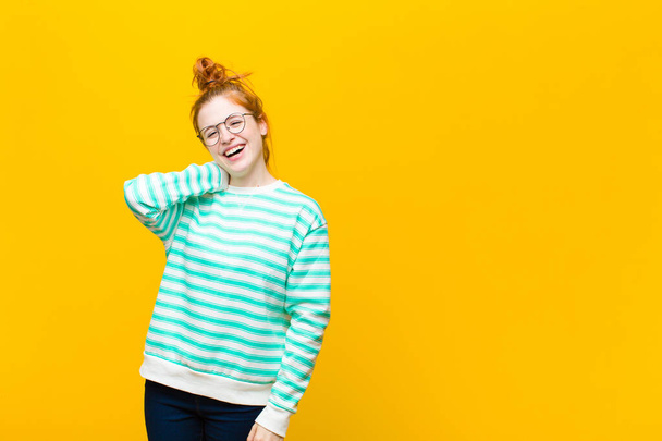 young red head woman laughing cheerfully and confidently with a casual, happy, friendly smile against orange wall - Photo, Image