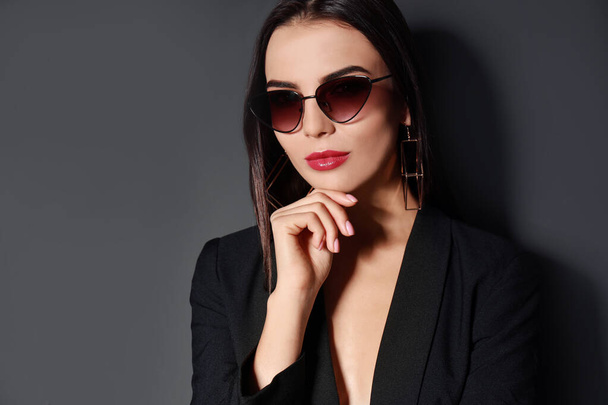 Beautiful woman wearing jacket and sunglasses on black background - Photo, Image