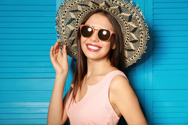 Beautiful woman wearing sunglasses and hat near blue wooden folding screen - Foto, Bild