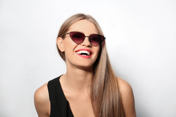Young woman wearing stylish sunglasses on light background - Fotografie, Obrázek