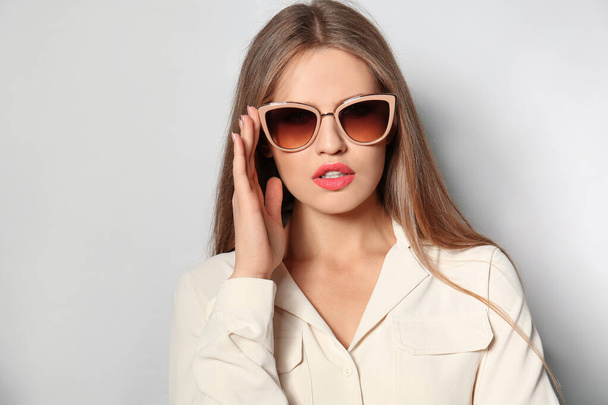 Young woman wearing stylish sunglasses on light background - Foto, afbeelding