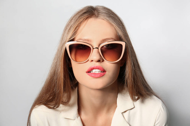 Young woman wearing stylish sunglasses on light background - Foto, afbeelding