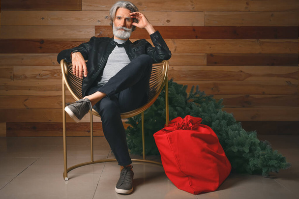 Portrait of stylish Santa Claus with Christmas tree and bag indoors - Фото, изображение