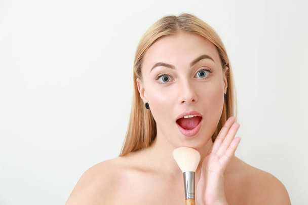 Hermosa mujer joven con cepillo de maquillaje sobre fondo claro
 - Foto, imagen