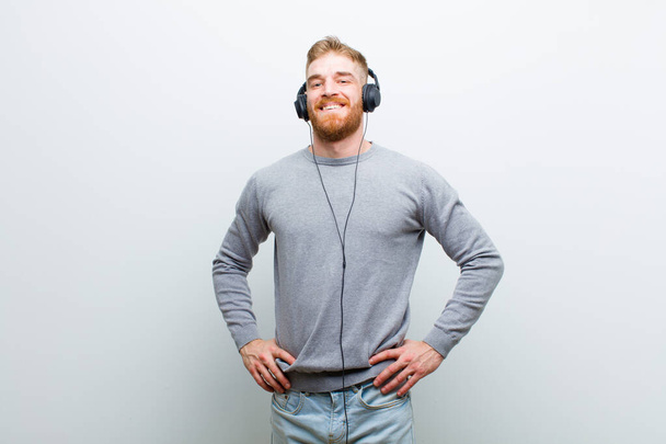 young red head man listening music with headphones against white background - Valokuva, kuva
