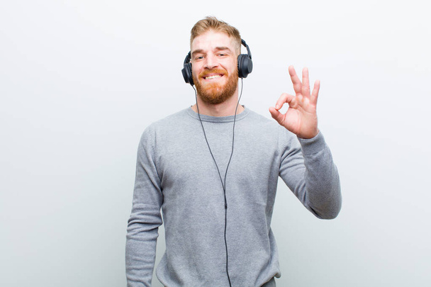 young red head man listening music with headphones against white background - Photo, image