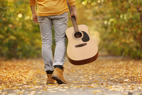 Young man with guitar walking in autumn park, closeup - 写真・画像