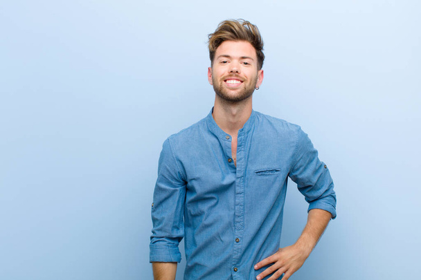 Молодой бизнесмен счастливо улыбается рукой на бедре и уверенно, позитивно, гордо и дружелюбно на синем фоне
 - Фото, изображение