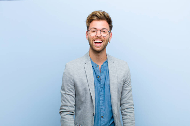 young businessman with a big, friendly, carefree smile, looking positive, relaxed and happy, chilling against blue background - Fotografie, Obrázek