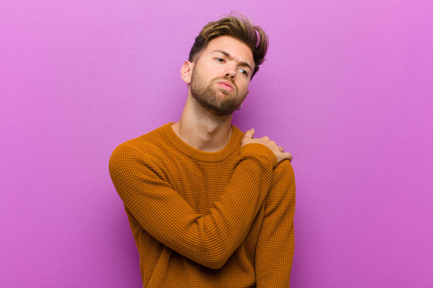 young man feeling anxious, ill, sick and unhappy, suffering a painful stomach ache or flu against purple background - Fotografie, Obrázek
