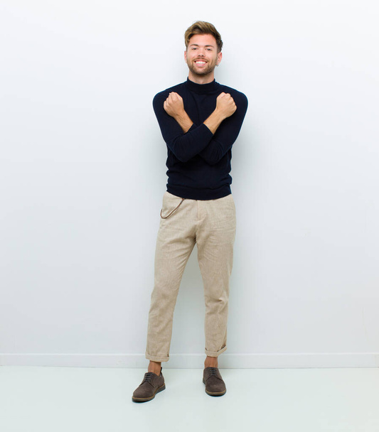 young full body man smiling cheerfully and celebrating, with fists clenched and arms crossed, feeling happy and positive against white background - Foto, immagini
