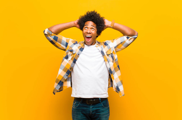 young black man looking happy, carefree, friendly and relaxed enjoying life and success, with a positive attitude against orange wall - Foto, afbeelding