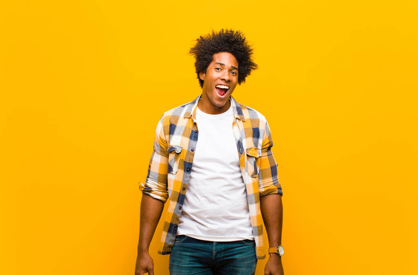 young black man with a big, friendly, carefree smile, looking positive, relaxed and happy, chilling against orange wall - Photo, image