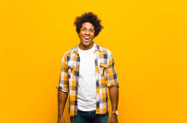 young black man looking happy and pleasantly surprised, excited with a fascinated and shocked expression against orange wall - Fotoğraf, Görsel