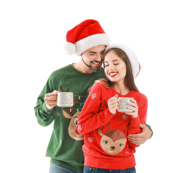 Happy young couple in Christmas clothes drinking hot chocolate on white background - Photo, Image