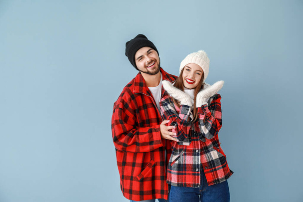 Ευτυχισμένο νεαρό ζευγάρι σε ζεστά χειμωνιάτικα ρούχα σε φόντο χρώματος - Φωτογραφία, εικόνα