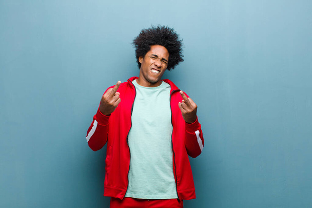 young black sports man feeling provocative, aggressive and obscene, flipping the middle finger, with a rebellious attitude against grunge wall - Fotoğraf, Görsel