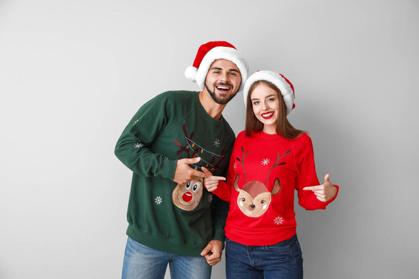 Happy young couple in Christmas clothes on light background - Photo, Image