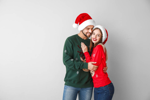 Ευτυχισμένο νεαρό ζευγάρι με Χριστουγεννιάτικα ρούχα στο φως φόντο - Φωτογραφία, εικόνα