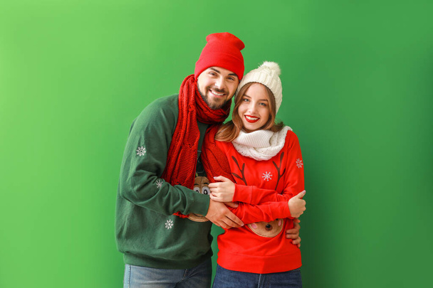 Happy young couple in Christmas clothes on color background - Photo, Image