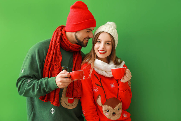 Happy young couple in Christmas clothes and with hot chocolate on color background - Фото, зображення