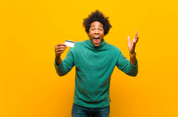 young african american man with a credit card against orange bac - Fotografie, Obrázek