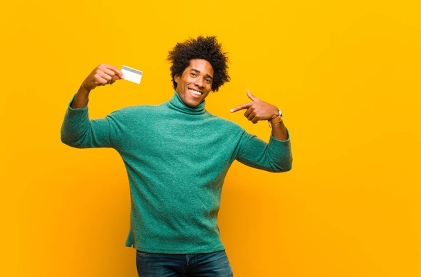 young african american man with a credit card against orange bac - Foto, afbeelding