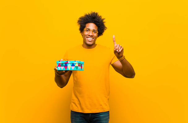 young african american man with a gift box against orange backgr - Foto, imagen