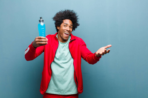 young black man with a sport drink against blue grunge wall - Foto, Imagen