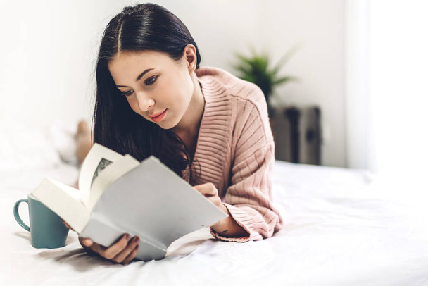 Молода жінка розслабляється і читає книгу на ліжку вдома
 - Фото, зображення