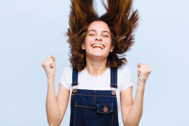 young pretty woman looking extremely happy and surprised, celebrating success, shouting and jumping against blue background - Φωτογραφία, εικόνα