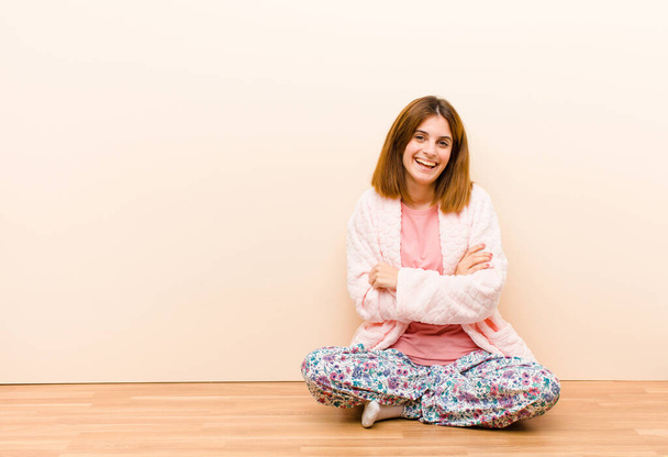 Pijama giyen genç bir kadın mutlu, gururlu ve tatmin olmuş görünüyor. Kollarını kavuşturup gülümsüyor. - Fotoğraf, Görsel