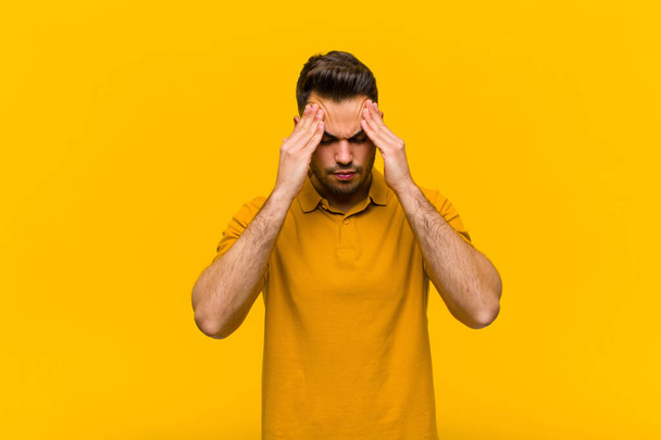 young hispanic man looking stressed and frustrated, working under pressure with a headache and troubled with problems against orange wall - Fotografie, Obrázek