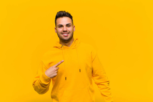young hispanic man looking proud, confident and happy, smiling and pointing to self or making number one sign against orange wall - Foto, Imagen